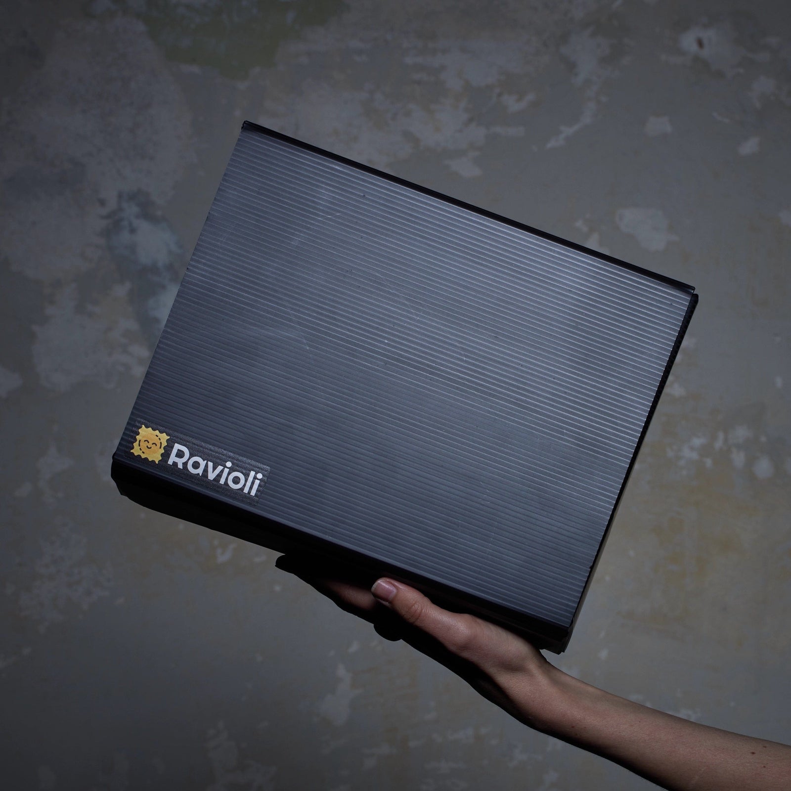 Foto einer schwarzen Ravioli-Verpackung von der Seite. Sie wird von einer Hand gehalten und das Ravioli Logo ist sichtbar.
